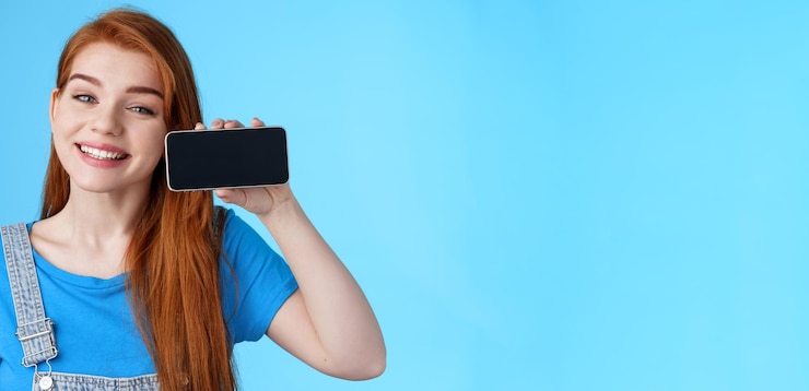 Photo gratuit gros plan joyeux étonné mignon rousse femelle look ravi tenir horizontal smartphone show applicati