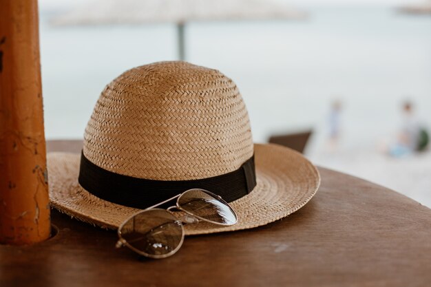 Gros plan d'une lunettes de soleil et d'un chapeau de paille sur une surface en bois
