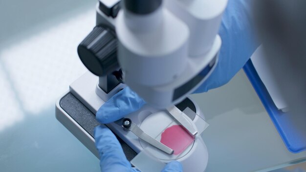 Gros plan de la main du médecin scientifique ajustant le microscope médical analysant la lame avec un échantillon de sang travaillant au développement d'un vaccin pendant l'expérience de chimie dans le laboratoire de l'hôpital. Notion de médecine