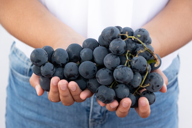 Gros plan d'une main d'homme tenant une grappe de raisins mûrs sur fond blanc