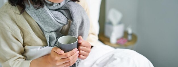 Photo gratuite gros plan des mains féminines tenant une boisson chaude allongée dans le lit, une fille attrape un rhume et reste à la maison