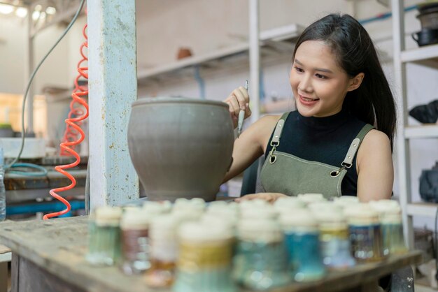 Gros plan sur des mains féminines travaillant sur des potiers wheelasian sculpture féminine femme colorant petit vase bol argile sur tour de potier à l'atelier home studio