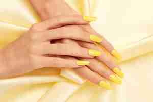 Photo gratuite gros plan sur les mains d'une femme avec du vernis à ongles jaune sur un tissu de soie jaune