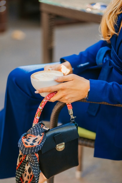 Photo gratuite gros plan des mains d'une femme élégante assise dans un café tenant un café et un petit sac à main élégant avec écharpe