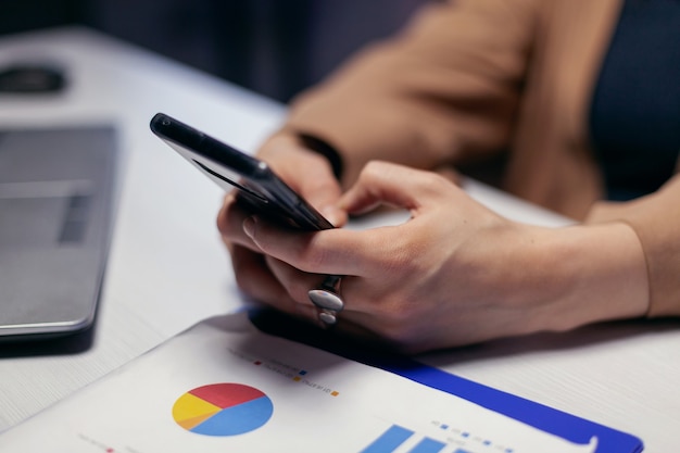 Photo gratuite gros plan des mains d'une femme entrepreneur à l'aide d'un téléphone intelligent au cours de la date limite. une femme d'affaires envoie des sms tard dans la nuit tout en travaillant sur un projet important à l'aide d'un smartphone.