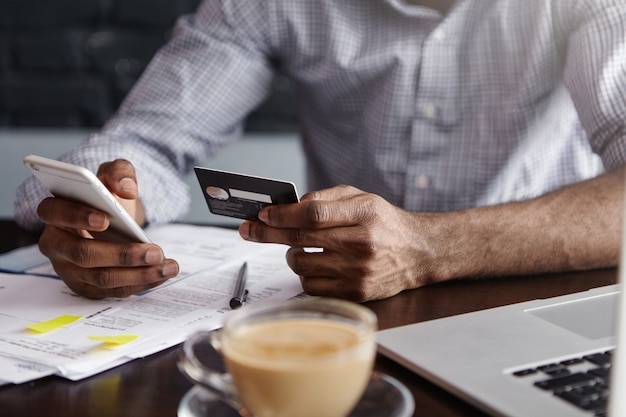 Gros plan des mains de l'homme africain tenant une carte de crédit et mobile