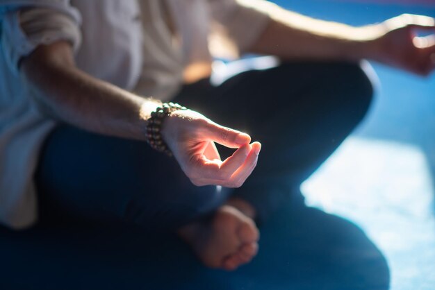 Gros plan sur les mains de l'homme méditant. Homme aux pieds nus assis en posture de lotus avec de la fumée autour de faire signe avec les doigts. Passe-temps, spiritualité, concept de santé