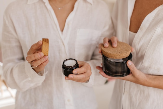 Gros plan sur les mains de jeunes femmes à la peau claire tenant des pots de crèmes pour le corps bio. Concept de soin et d'hydratation