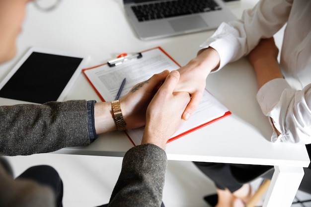 Gros plan sur des mains masculines et féminines tenant à la table avec des feuilles de bureau pour smartphone pour ordinateur portable