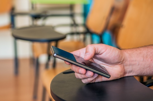 Gros plan des mains masculines tenant le téléphone portable et la classe. Homme utilisant un smartphone mobile. Garçon touchant un écran de son smarthone. Fond flou, horizontal.