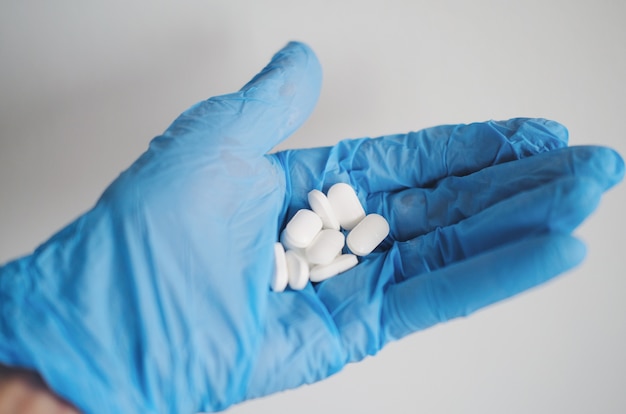 Gros plan des mains d'une personne portant des gants bleus et tenant des pilules blanches