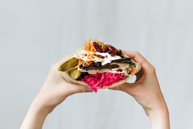 Photo gratuite gros plan de mains tenant un shawarma végétarien avec des haricots rouges et des cornichons enveloppés dans du pain pita