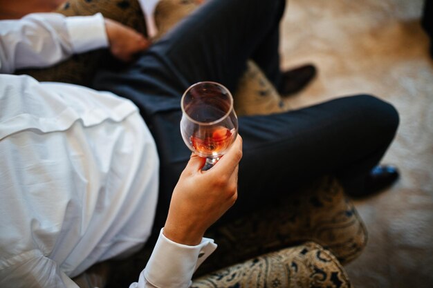 Gros plan sur un marié méconnaissable dégustant un verre de vin rouge le jour de son mariage