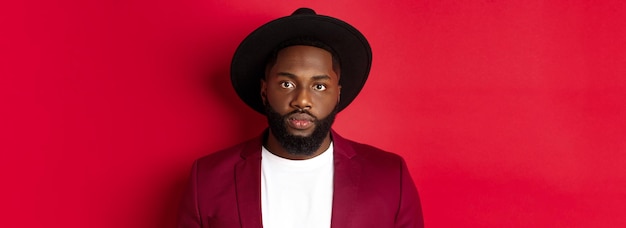 Photo gratuite gros plan d'un mec afro-américain sérieux en blazer et chapeau noir regardant la caméra debout vo