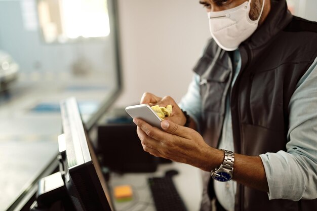 Gros plan d'un mécanicien automobile désinfectant un téléphone intelligent tout en travaillant au bureau de l'atelier de réparation