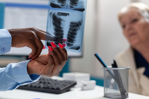 Photo gratuite gros plan d'un médecin thérapeute tenant une radiographie pulmonaire expliquant l'expertise de la maladie à une femme handicapée âgée malade en fauteuil roulant lors d'une consultation médicale au bureau de l'hôpital. notion de médecine