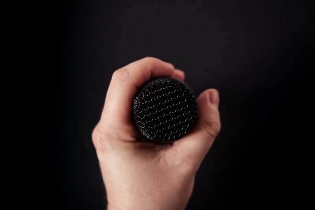 Gros plan d'un microphone dans la main d'une personne sur fond noir