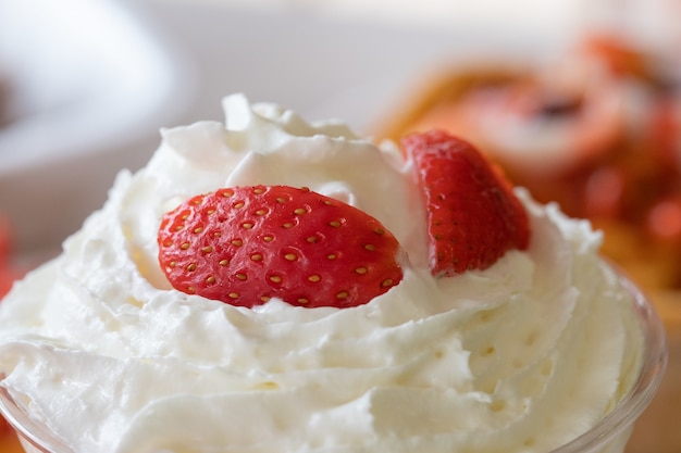 Gros plan de mise au point sélective de crème fouettée avec des fraises fraîches