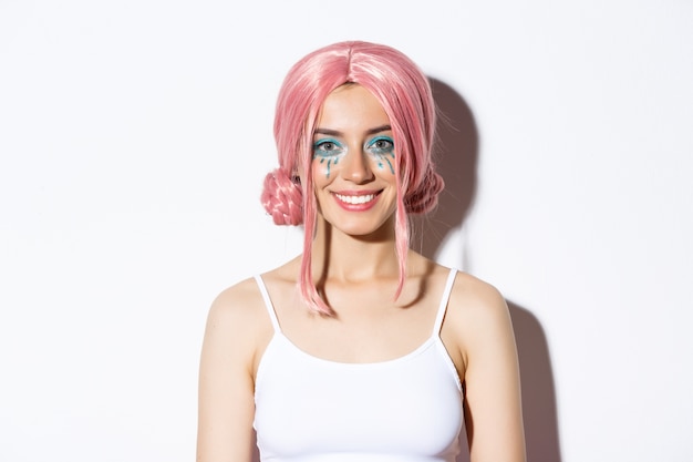 Gros plan d'un modèle assez féminin en perruque rose, maquillage coloré, habillé pour la fête d'halloween, debout.