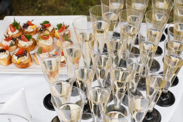 Gros plan sur de nombreuses flûtes de champagne ou autre boisson gazeuse avec toasts aux légumes et fromage à la crème lors d'une réception de mariage ou d'un banquet. Réception festive.