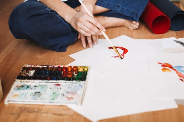 Gros plan peintre assis sur le sol et dessin à l'aquarelle sur papier à la maison