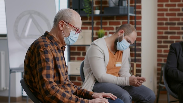 Photo gratuite gros plan sur une personne âgée parlant de la toxicomanie et de l'alcoolisme lors d'une séance de thérapie de groupe. homme senior discutant avec des personnes lors d'une réunion de réadaptation pendant la pandémie de coronavirus.