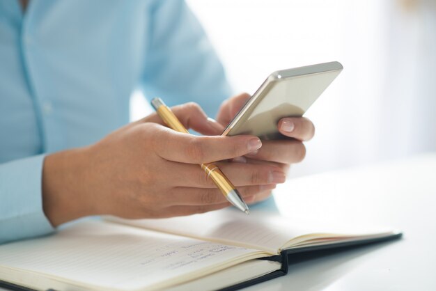 Gros plan d&#39;une personne à l&#39;aide de smartphone et travaillant à table