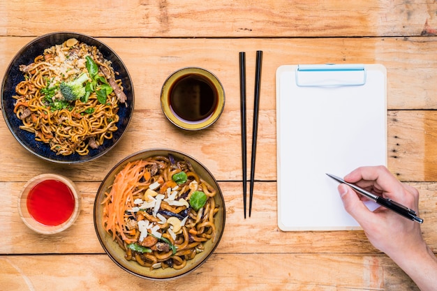 Gros plan, personne, écriture, presse-papiers, stylo, près, thaï, traditionnel, nourriture, sauces, table