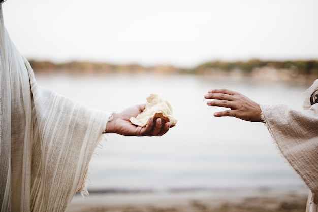 Gros plan d'une personne portant une robe biblique donnant du pain à une autre personne