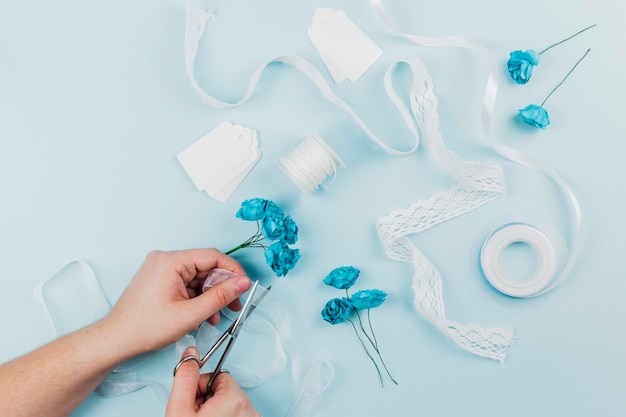 Gros plan d&#39;une personne qui coupe le ruban avec des ciseaux pour attacher les roses bleues sur fond coloré