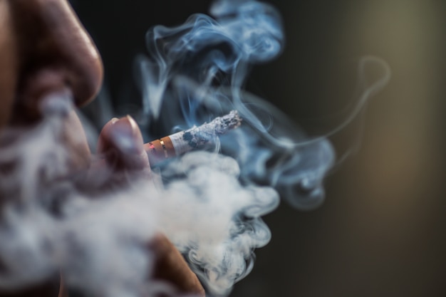 Gros plan d'une personne soufflant sur une cigarette entourée de fumée
