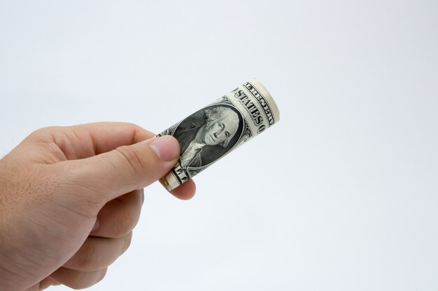 Gros plan d'une personne tenant un billet d'un dollar plié sur un mur gris
