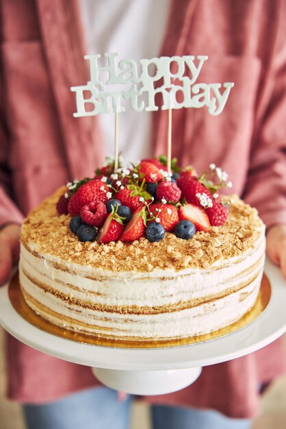 Gros plan d'une personne tenant le gâteau fruité avec un topper "Happy Birthday"