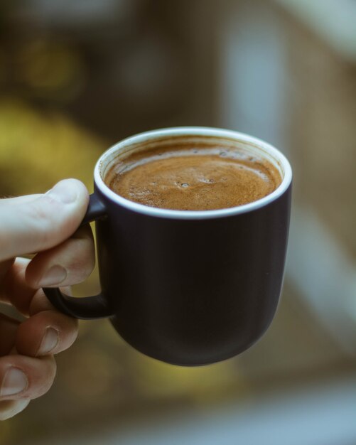 Gros plan d'une personne tenant une tasse de café noir
