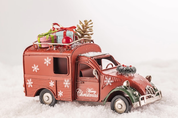 Gros plan d'une petite voiture avec des ornements de Noël sur elle sur la neige artificielle sur un fond blanc