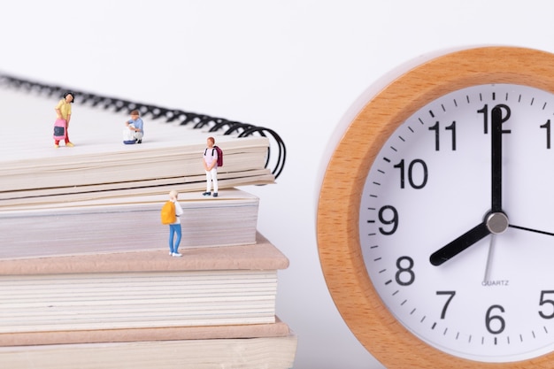 Gros plan sur de petites figurines d'étudiants debout sur des manuels à côté d'une horloge