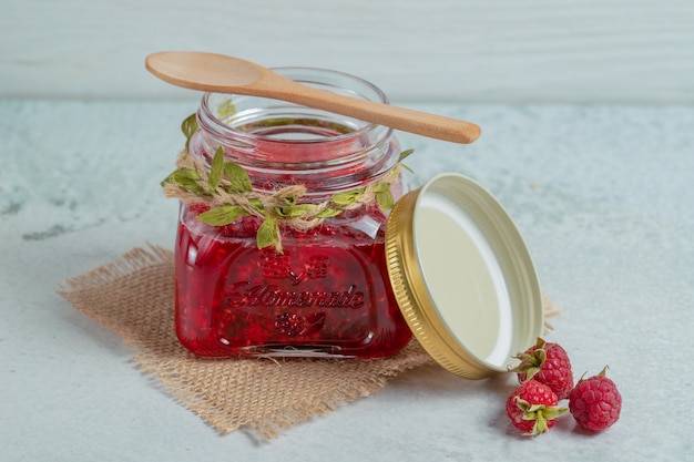 Gros plan photo de confiture maison et framboise fraîche sur une surface grise.