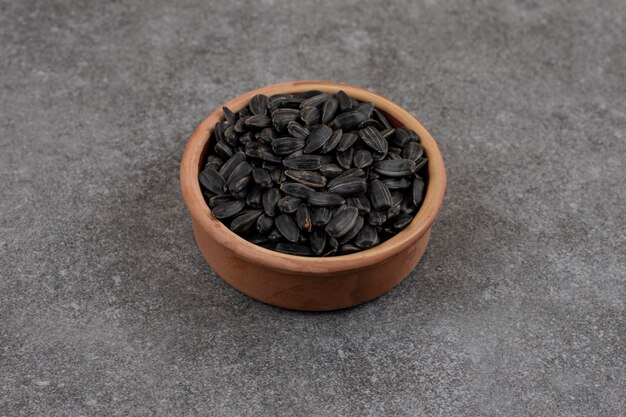 Gros plan photo. Tas de graines de tournesol dans un bol de poterie sur une surface grise.