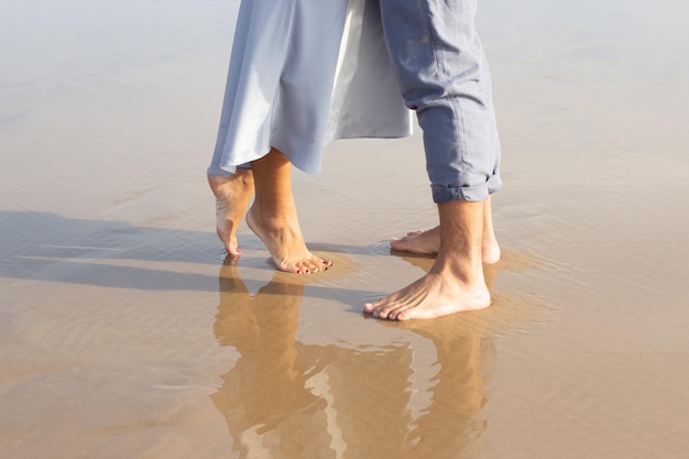 Gros plan des pieds nus masculins et féminins sur le sable humide. Homme et femme marchant sur la plage avec un bord de vagues moussant doucement en dessous. Vacances, concept de bonheur