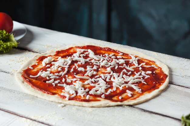 Photo gratuite gros plan d'une pizza crue faite maison avec du fromage et de la sauce tomate sur un fond en bois