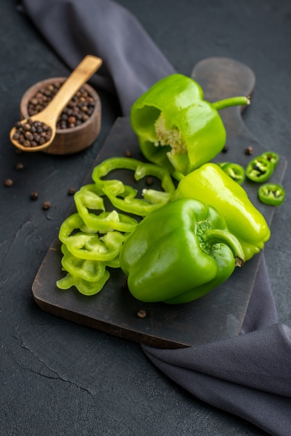 Photo gratuite gros plan de poivrons verts coupés entiers coupés sur une planche à découper en bois sur une surface de couleur sombre