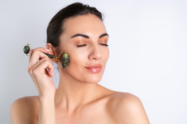 Gros plan portrait de beauté d'une femme avec une peau parfaite et des lèvres nues charnues de maquillage naturel tenant un masseur à rouleaux pour le visage et le coux9