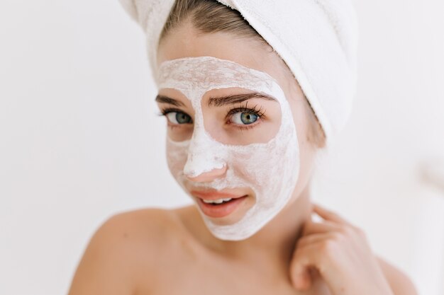 Gros plan portrait de la belle jeune femme avec des serviettes après prendre le bain faire un masque cosmétique sur son visage.