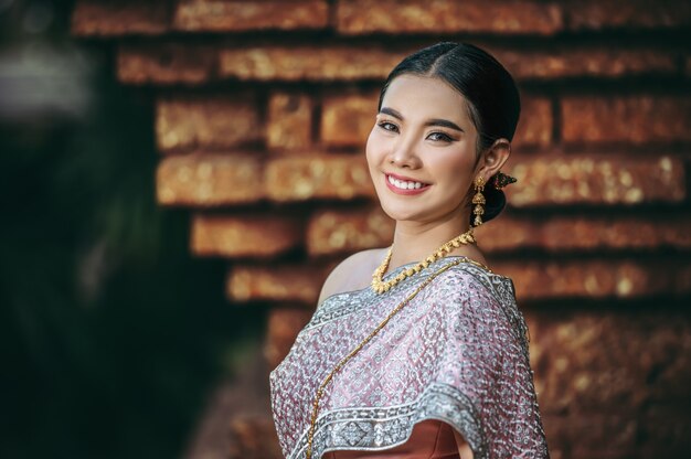 Gros plan, Portrait charmante femme asiatique vêtue d'une belle robe thaïlandaise typique dans un temple antique ou un lieu célèbre avec une pose gracieuse