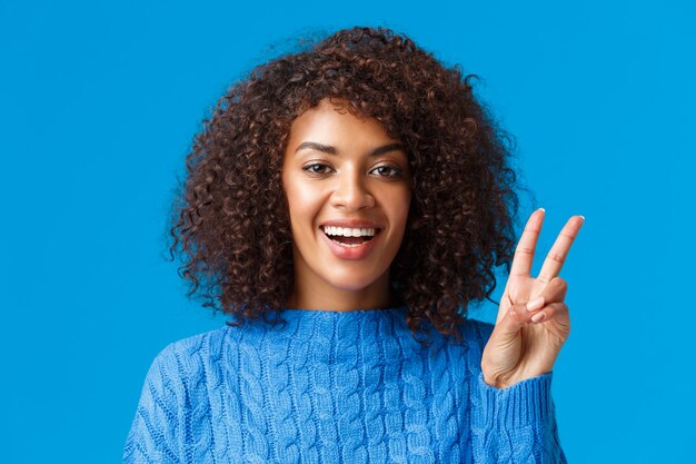 Gros plan portrait insouciant, femme joyeuse heureuse célébrant les vacances, souhaitant à tous une bonne année, montrant le signe de la paix et souriant joyeusement, exprimez la posivité et la joie, portant un pull.