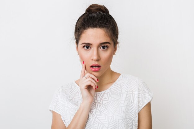 Gros plan portrait de jeune femme choquée en chemisier blanc a ouvert la bouche, tenant le doigt sur son visage, expression du visage surpris, ayant un problème isolé