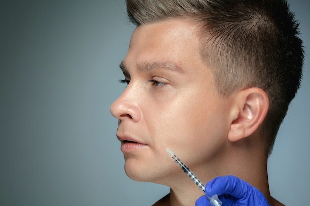 Photo gratuite gros plan portrait de jeune homme isolé sur mur gris studio en procédure de chirurgie de remplissage