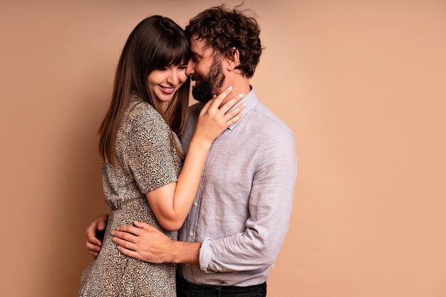 Gros plan portrait en studio d'un couple amoureux d'âge moyen, câlins et bisous, heureux ensemble, tenues de soirée glamour, prêt pour la célébration, fond beige.