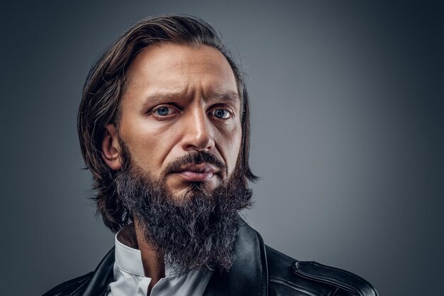 Gros plan portrait en studio d'un homme sérieux et barbu sur fond gris.