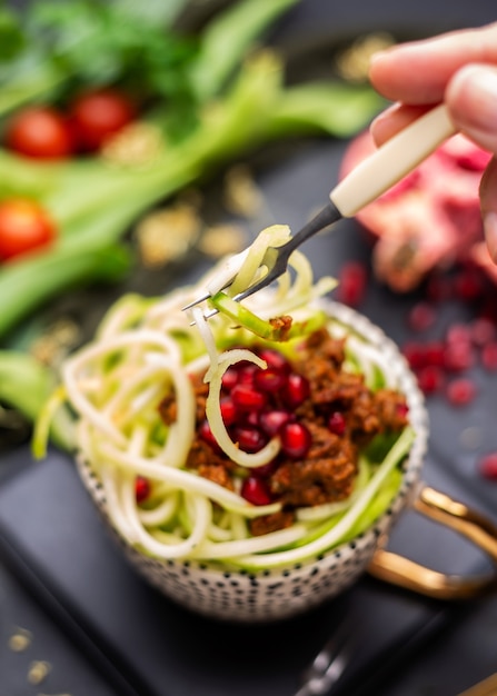 Gros plan d'un repas végétalien avec des courgettes en spirale, de la sauce tomate et des grenades dans la tasse